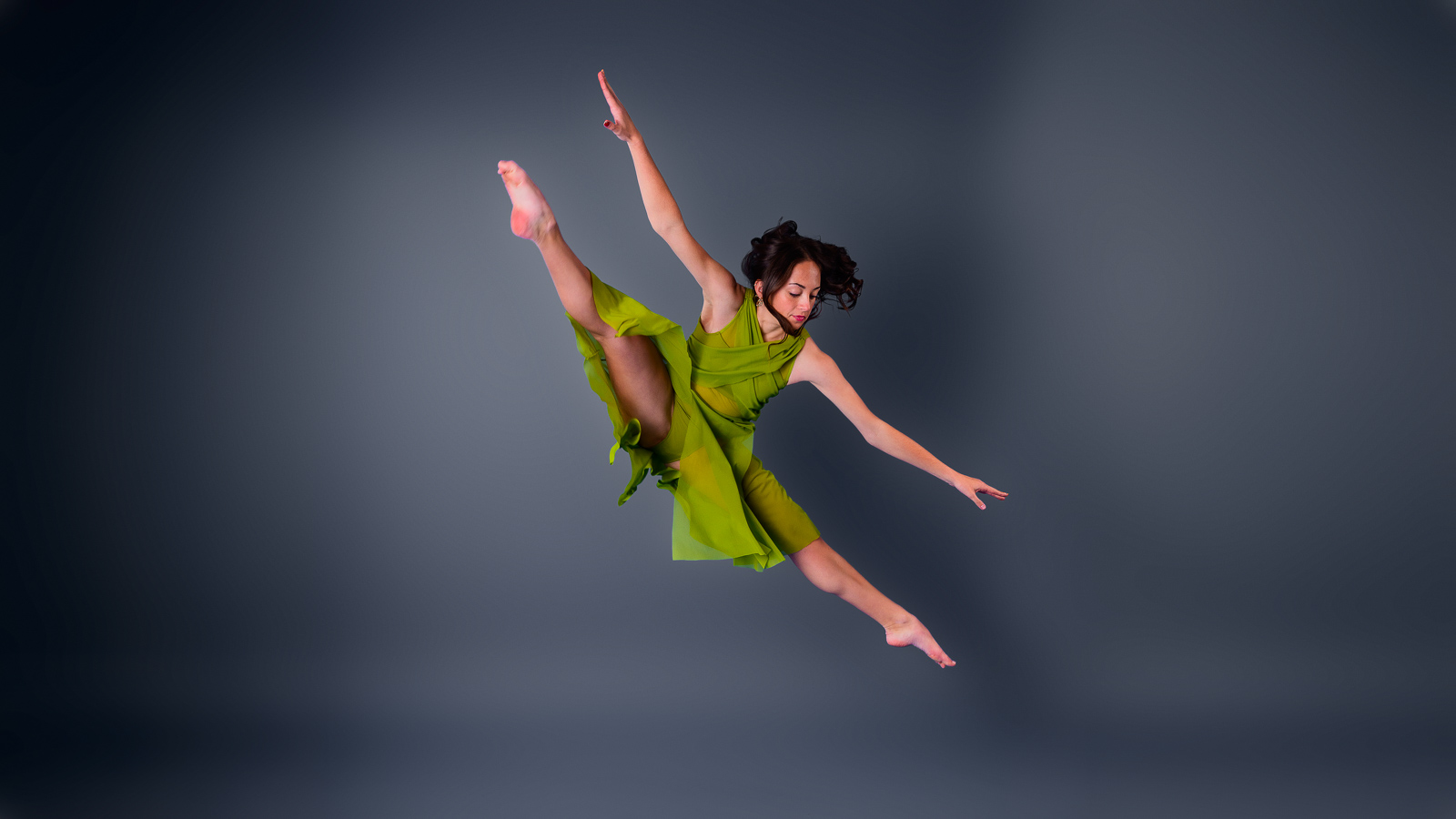 Dancer in a green dress leaping through the air in a studio portrait