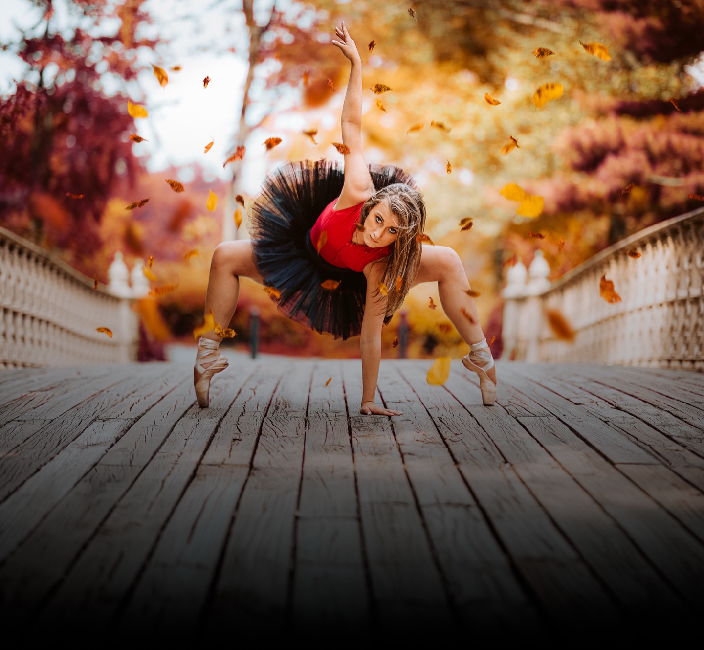 Ballet dancer posing on pointe on a bridge surrounded by autumn leaves