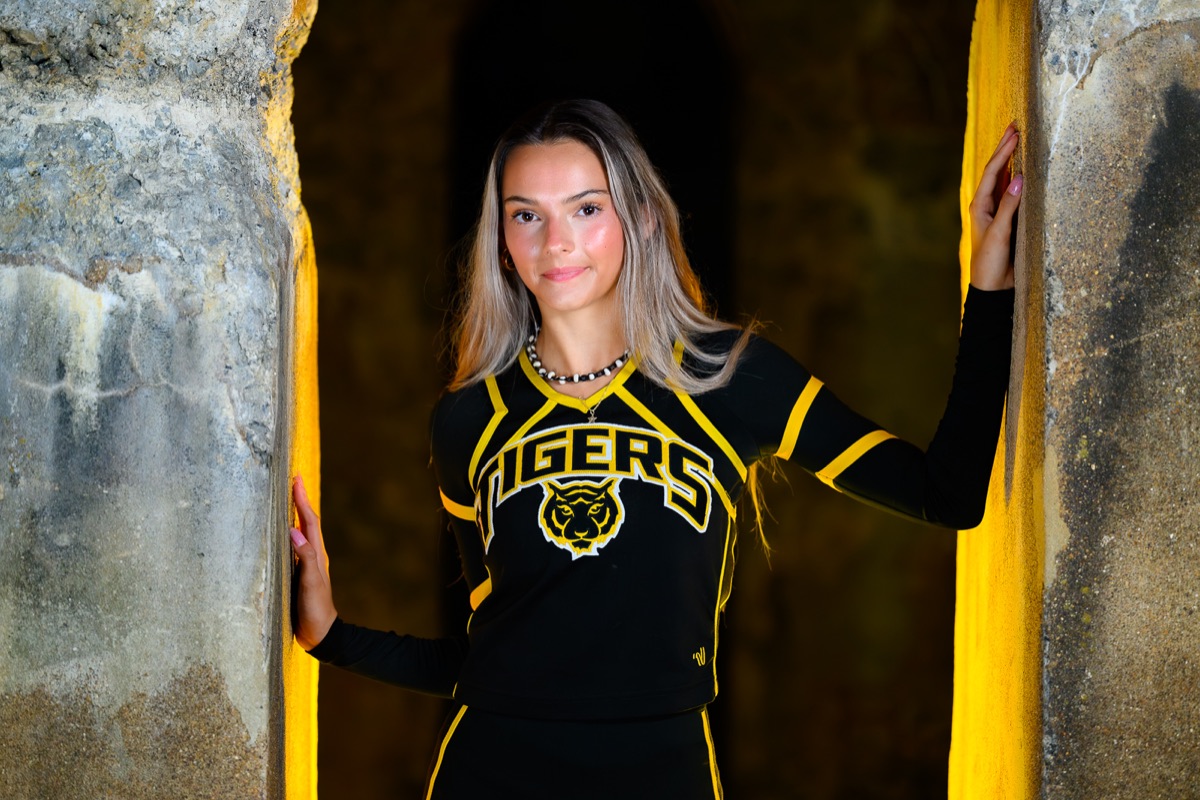 Senior portrait in a black and gold Tigers uniform framed by stone architecture