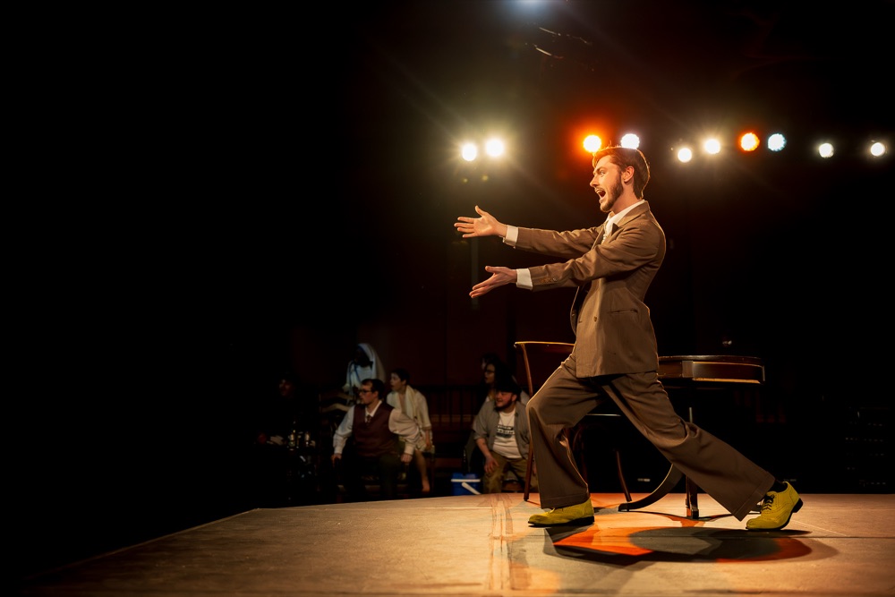 Actor in a suit delivering a monologue under warm stage lights
