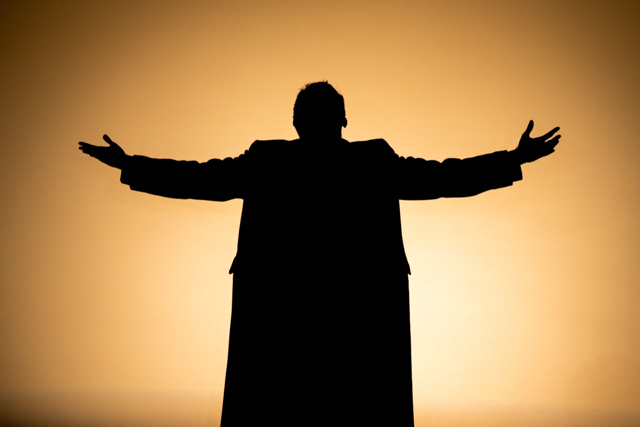 Silhouette of a performer with arms outstretched against warm theatrical light